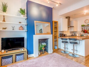 A modern kitchen with a blue accent wall, a fireplace, a TV, and a bar area with stools.