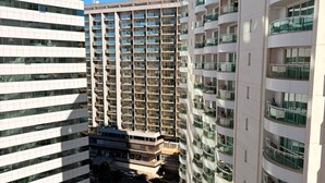 A high-rise building with multiple balconies, a parking area, and a clear sky. - Saint Moritz  no coração de Brasília (Brasília)