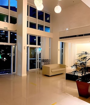 A spacious interior with a high ceiling, a sofa, a potted plant, and a sliding glass door leading to an outdoor area. - Saint Moritz  no coração de Brasília (Brasília)