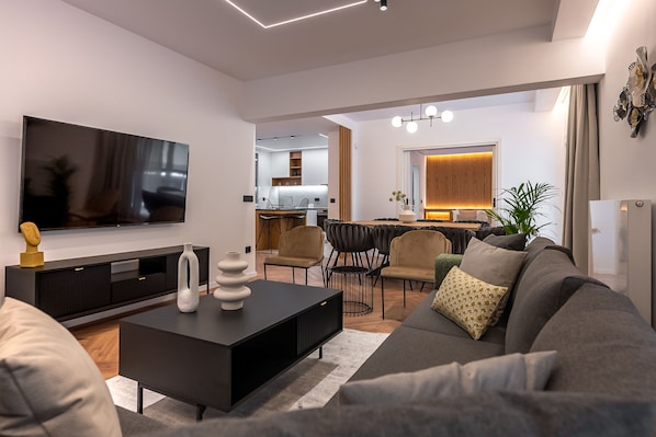 A modern living room with a flat-screen TV, a dark coffee table, and a grey sofa.