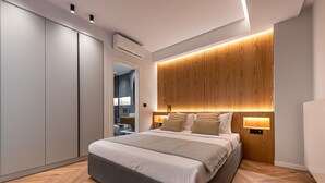 A modern bedroom with a large bed, built-in wooden headboard, bedside lamps, and a wardrobe. - Phaedrus Living: Luxury Penthouse Ploutarchou (Athens)
