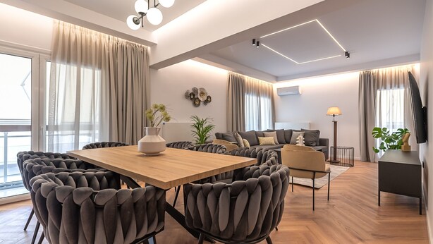 A modern living room with a wooden dining table, plush chairs, a sofa, and a TV mounted on the wall. - Phaedrus Living: Luxury Penthouse Ploutarchou (Athens)