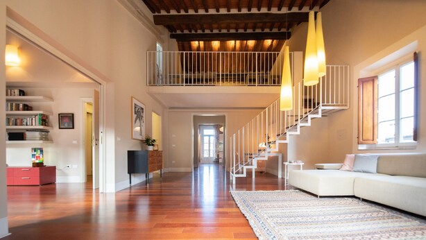 A spacious living area with hardwood flooring, a white sofa, a patterned rug, and a staircase with a railing. - Casa della Luce Luxury in Center Town (Lucca)