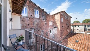 A balcony with a table and chairs, overlooking a courtyard with a tiled roof and a brick building. - Casa della Luce Luxury in Center Town (Lucca)