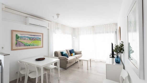 Ein modernes Wohnzimmer mit Essbereich, einer Couch mit Kissen, einem Couchtisch und einem Gemälde an der Wand.