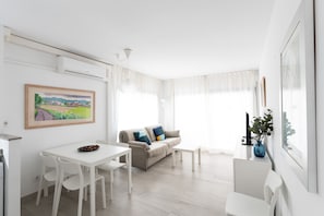 A modern living room with a dining area, a sofa with cushions, a coffee table, and a painting on the wall.