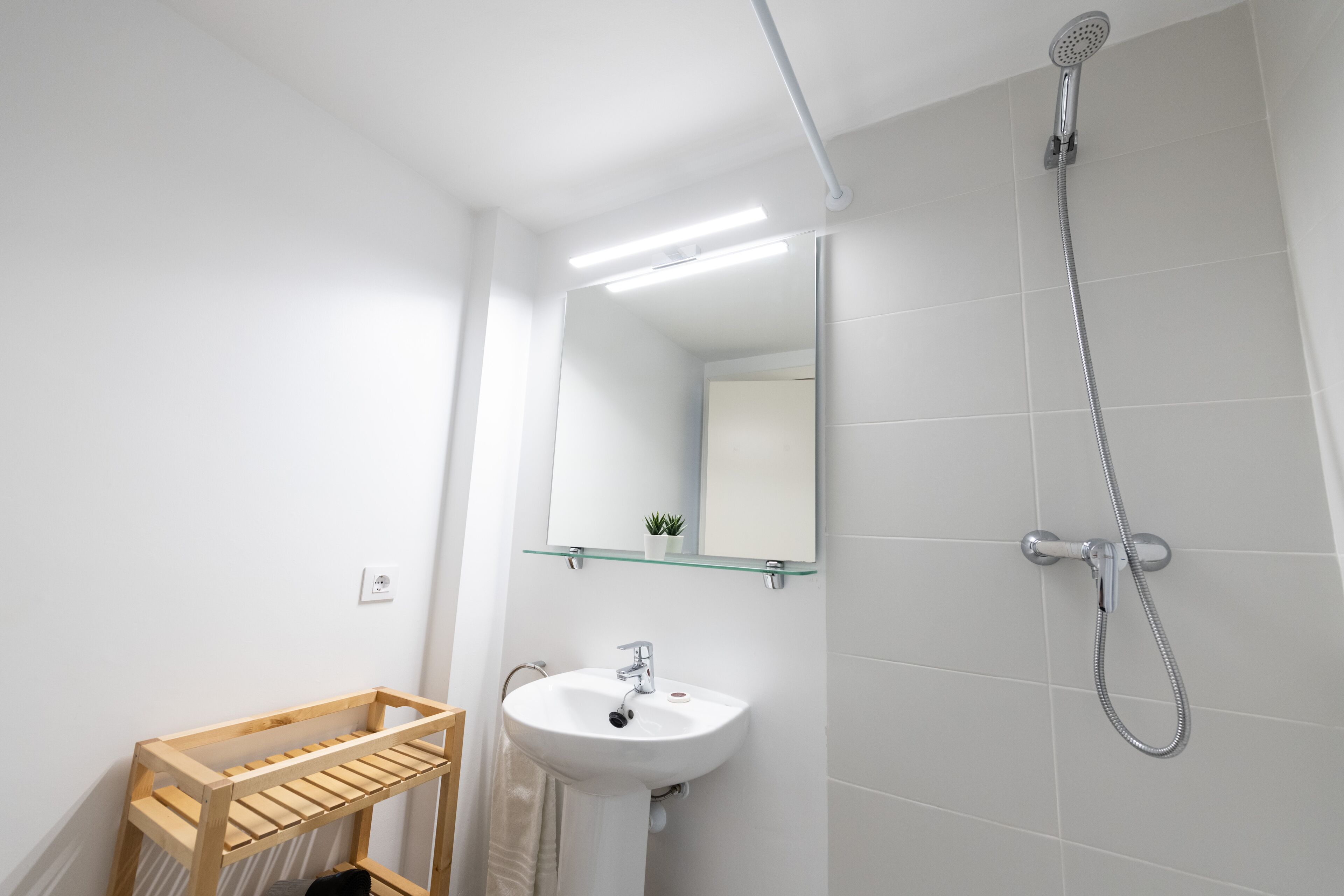 Ein modernes Badezimmer mit Holzregal, Waschbecken, Spiegel und Dusche.