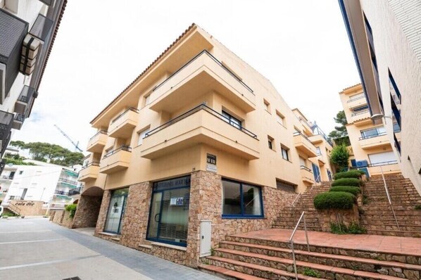 A multi-story residential building with balconies, stone facade, and a staircase leading to the entrance.