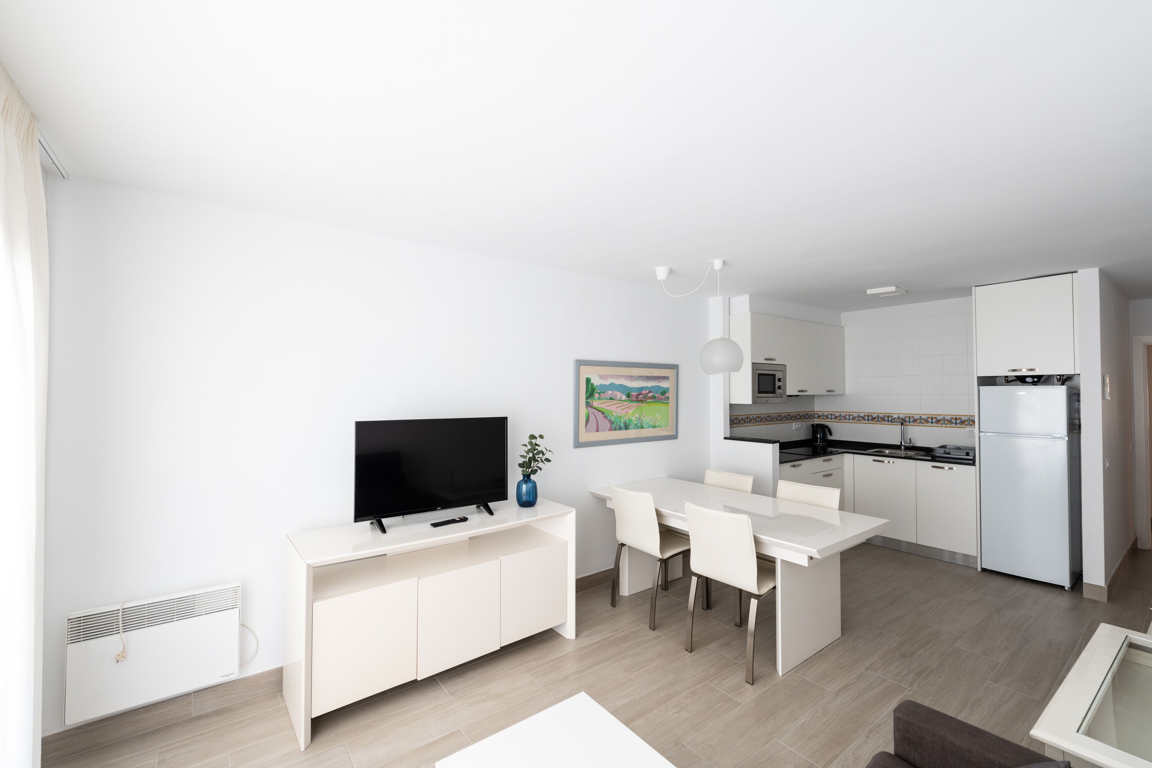 Ein moderner, minimalistischer Wohnraum mit Essbereich, Küche und einem Flachbildfernseher.