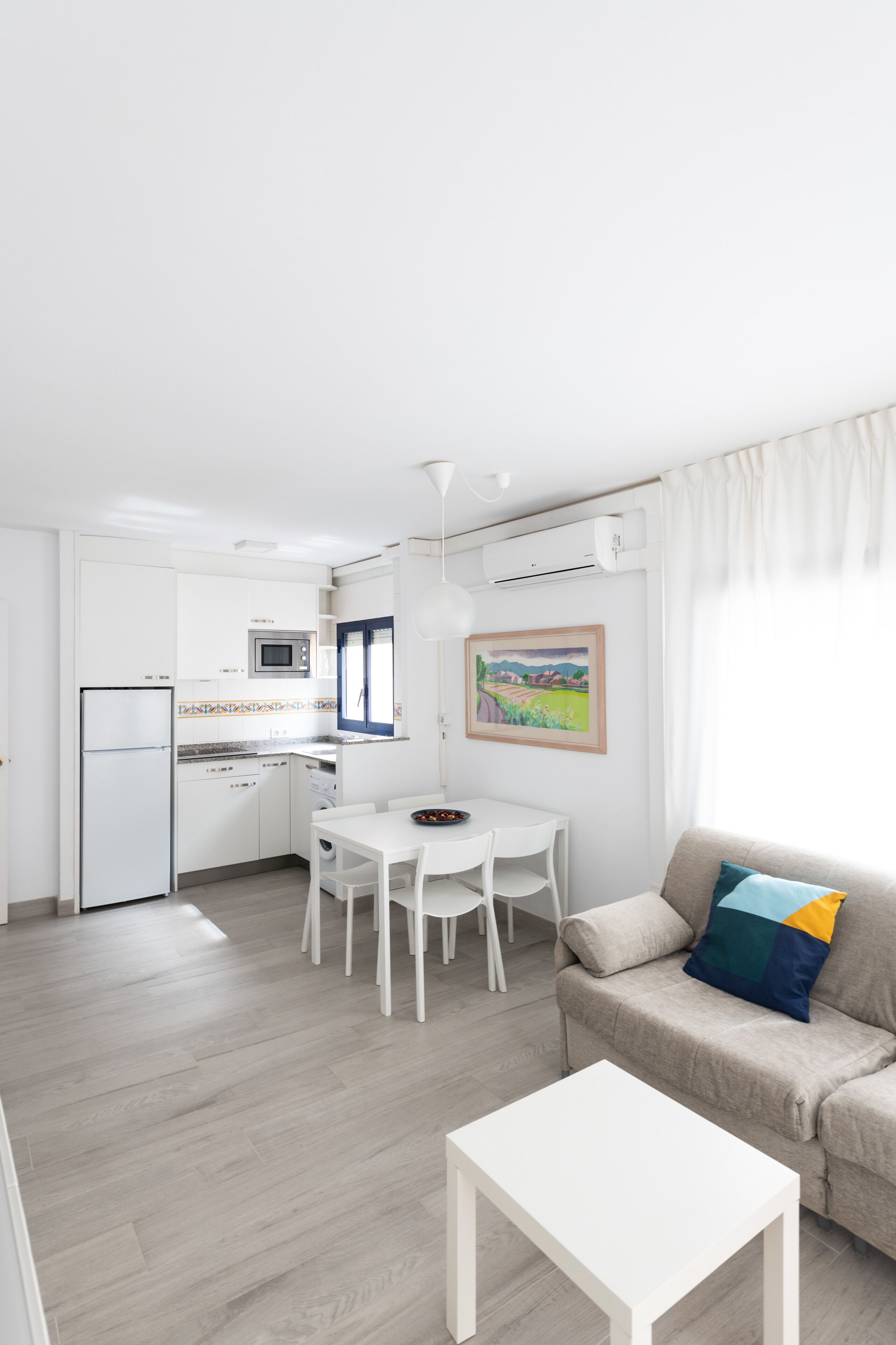 Un salon moderne avec un canapé blanc, une petite table blanche et un coin repas comprenant une table et des chaises blanches.