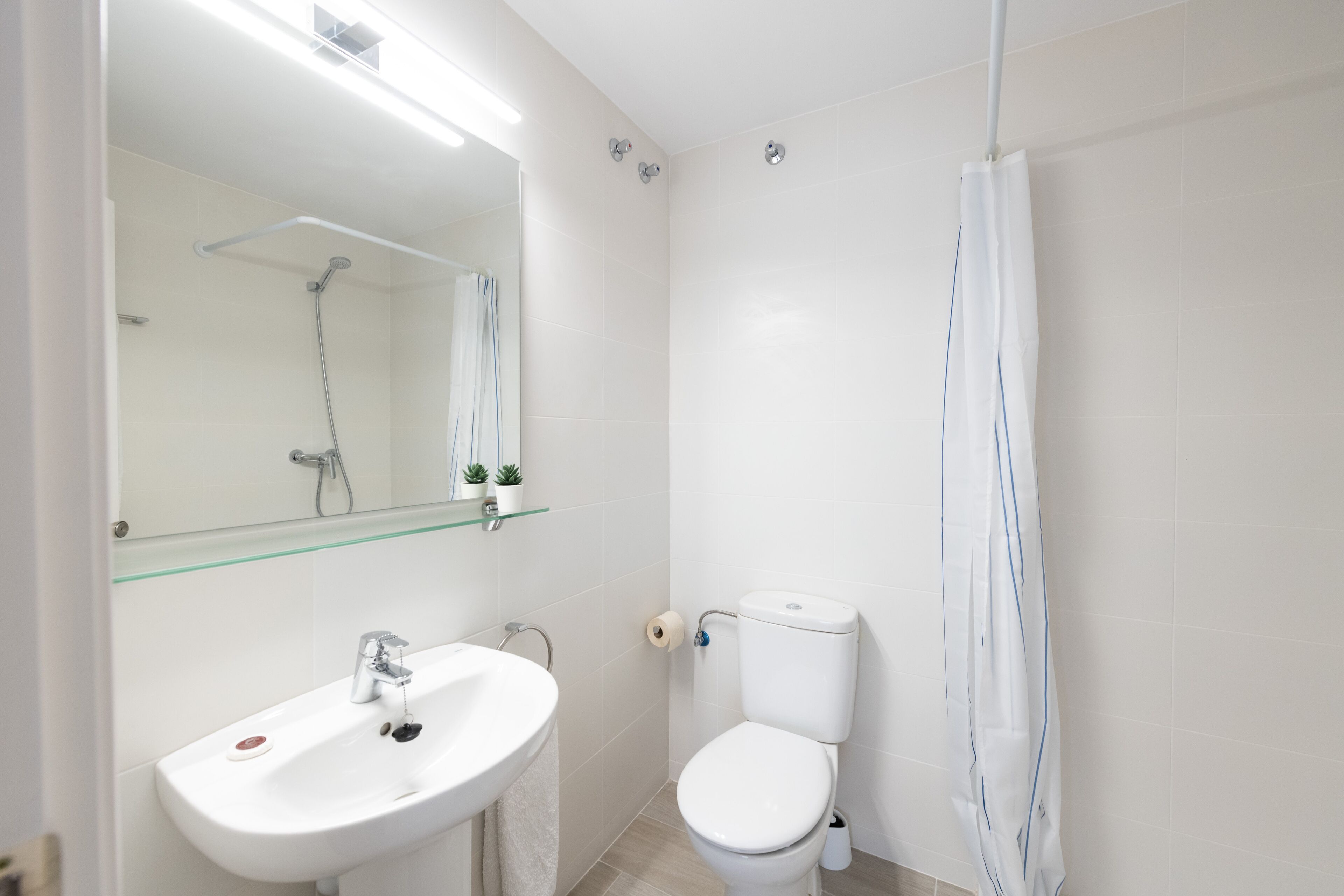 Un baño moderno con lavamanos, inodoro y cortina de ducha blancos.