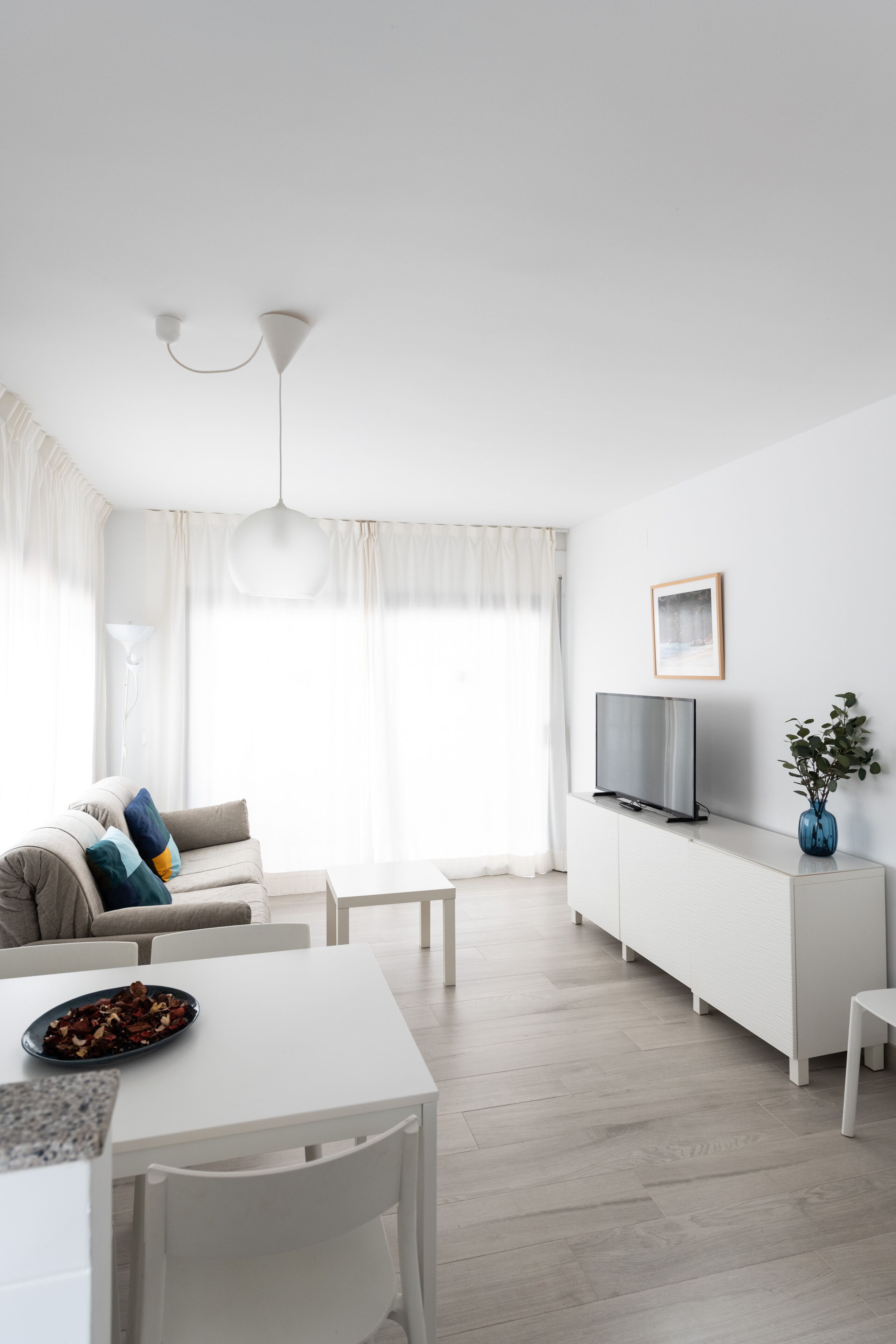 Una sala de estar moderna con un sofá blanco, una mesa de comedor y un televisor sobre un mueble blanco.
