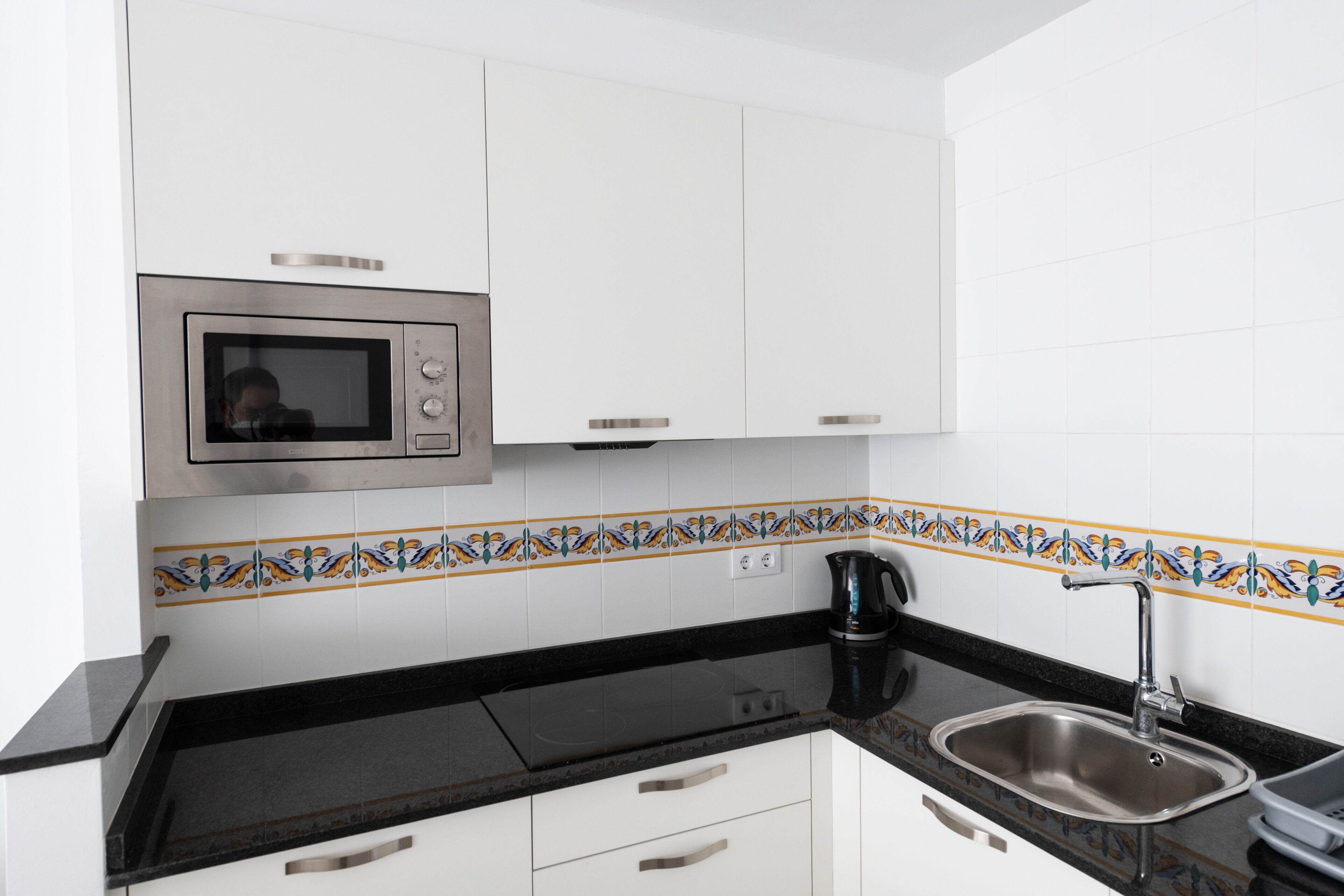 A kitchen with white cabinets, a stainless steel microwave, a black countertop, and a sink.