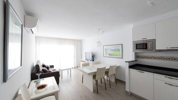 A modern kitchen with white cabinets, a black countertop, and a microwave. There is a dining area with a white table and chairs.