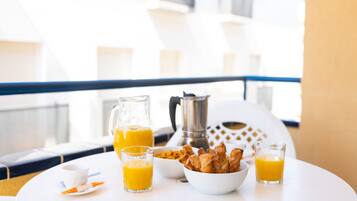 Ein Esstisch mit Orangensaft, einer Kaffeekanne und einer Schale Gebäck auf einem Balkon.