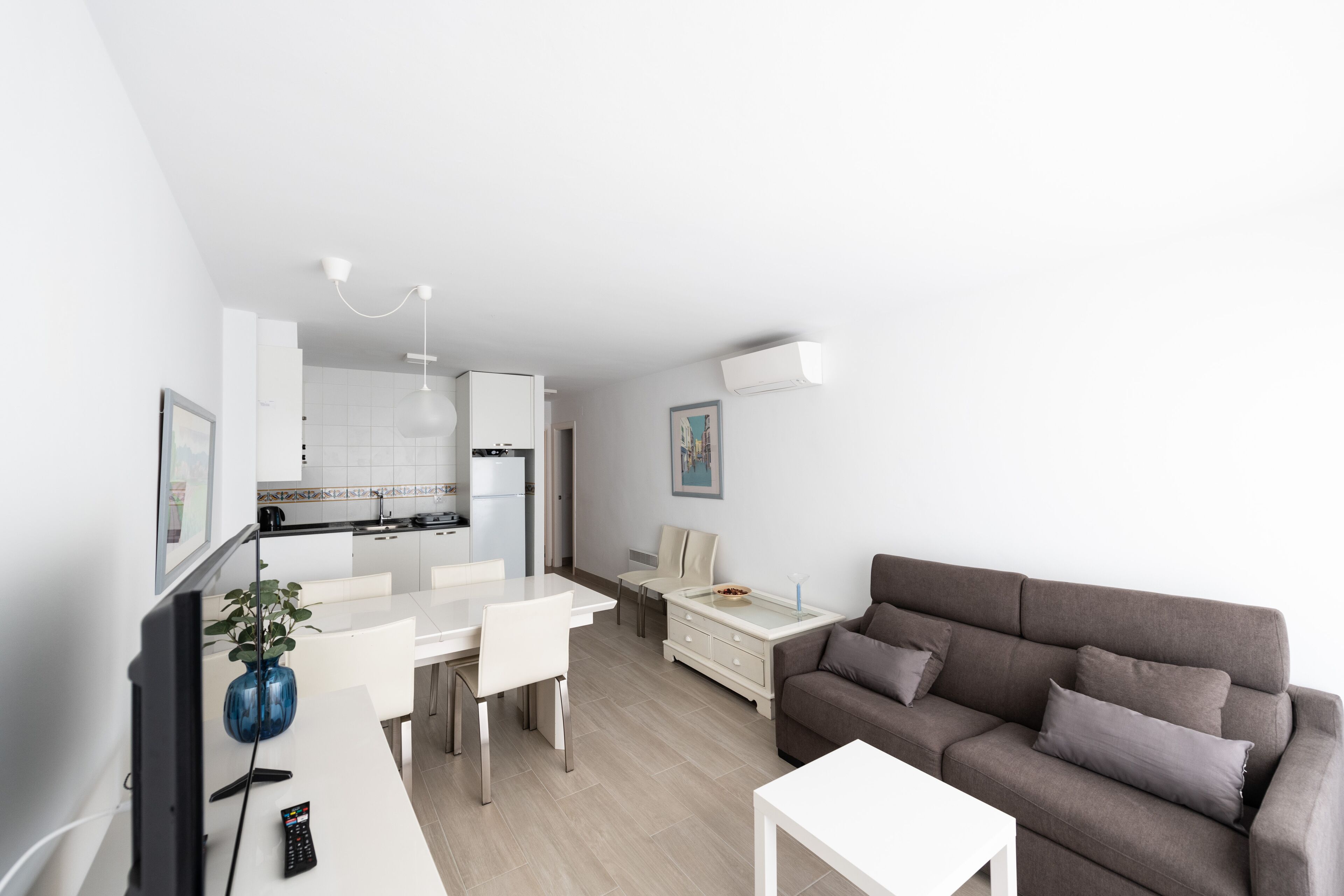 Een moderne woonkamer met een grijze bank, een witte salontafel en een eethoek met een witte tafel en stoelen.