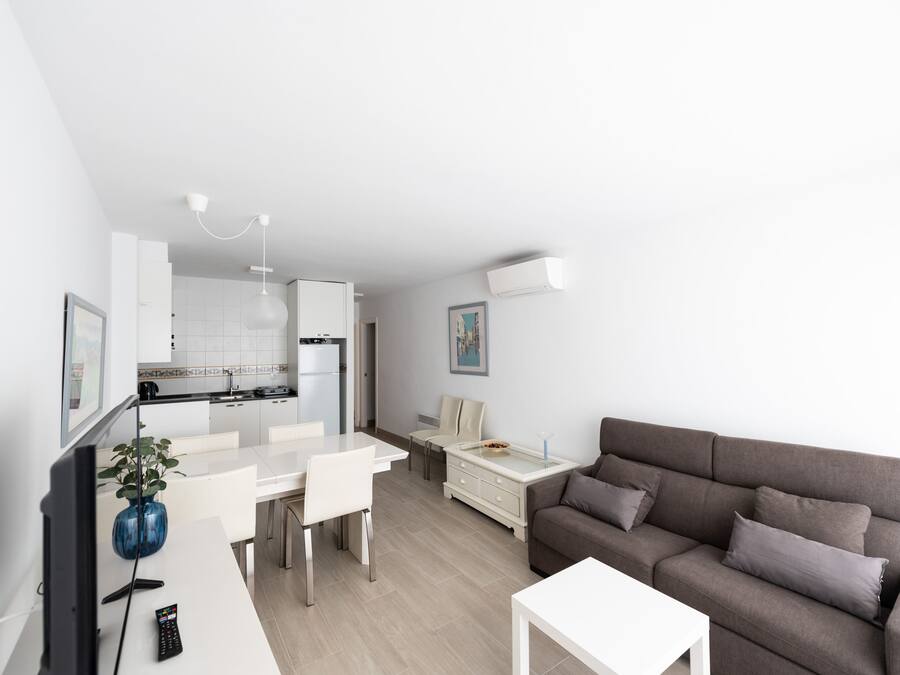 Ett modernt vardagsrum med en grå soffa, ett vitt soffbord och en matplats med ett vitt bord och stolar.