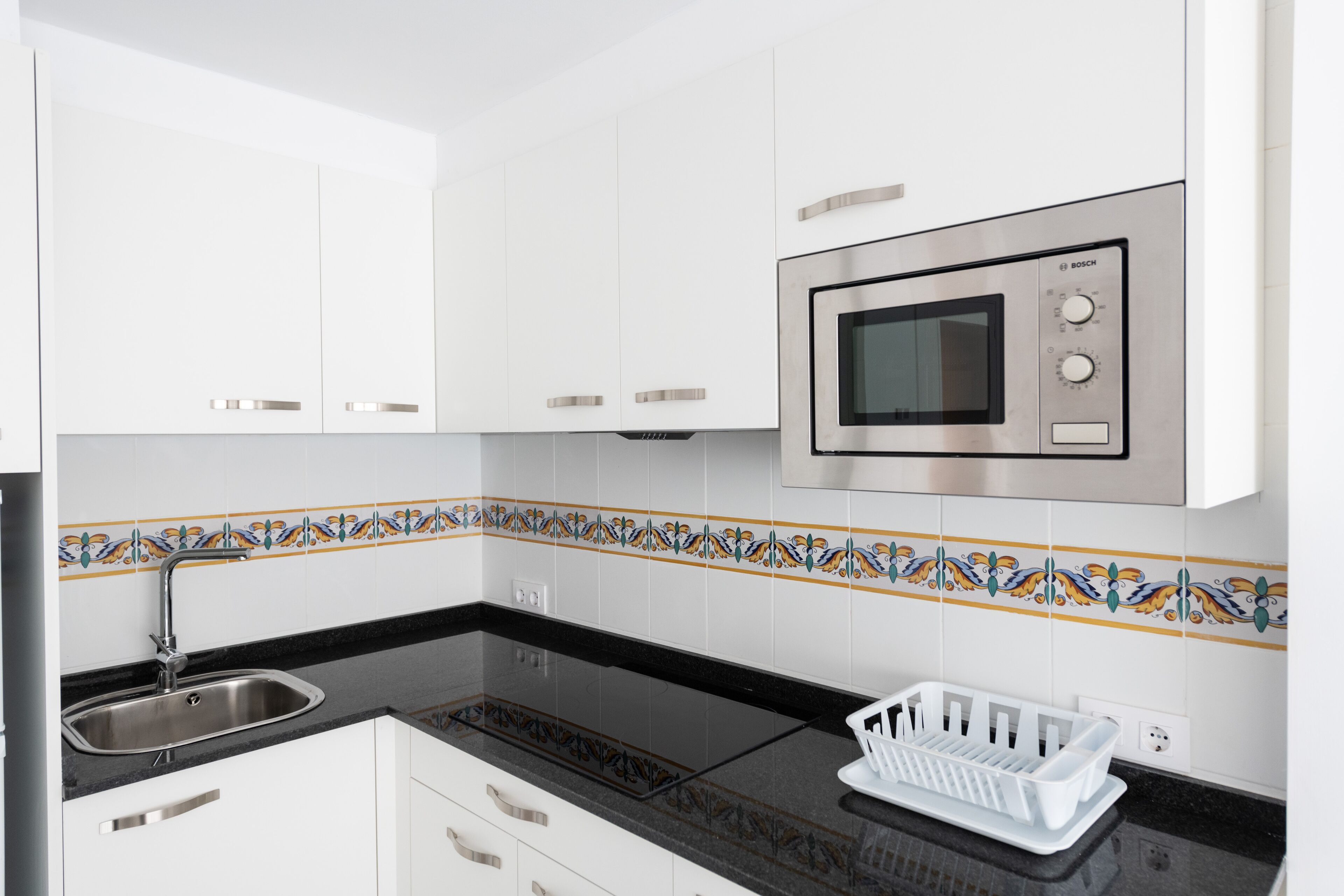 A modern kitchen with white cabinets, a stainless steel microwave, a black countertop, and a decorative tile backsplash.