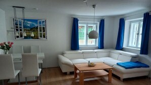 Ein modernes Wohnzimmer mit einem weißen Sofa, einem Holztisch und einem Essbereich mit weißen Stühlen und einem Tisch.