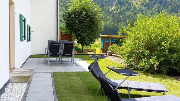 Eine Terrasse mit Sitzgelegenheit, einem kleinen Tisch und Blick auf eine gebirgige Landschaft.
