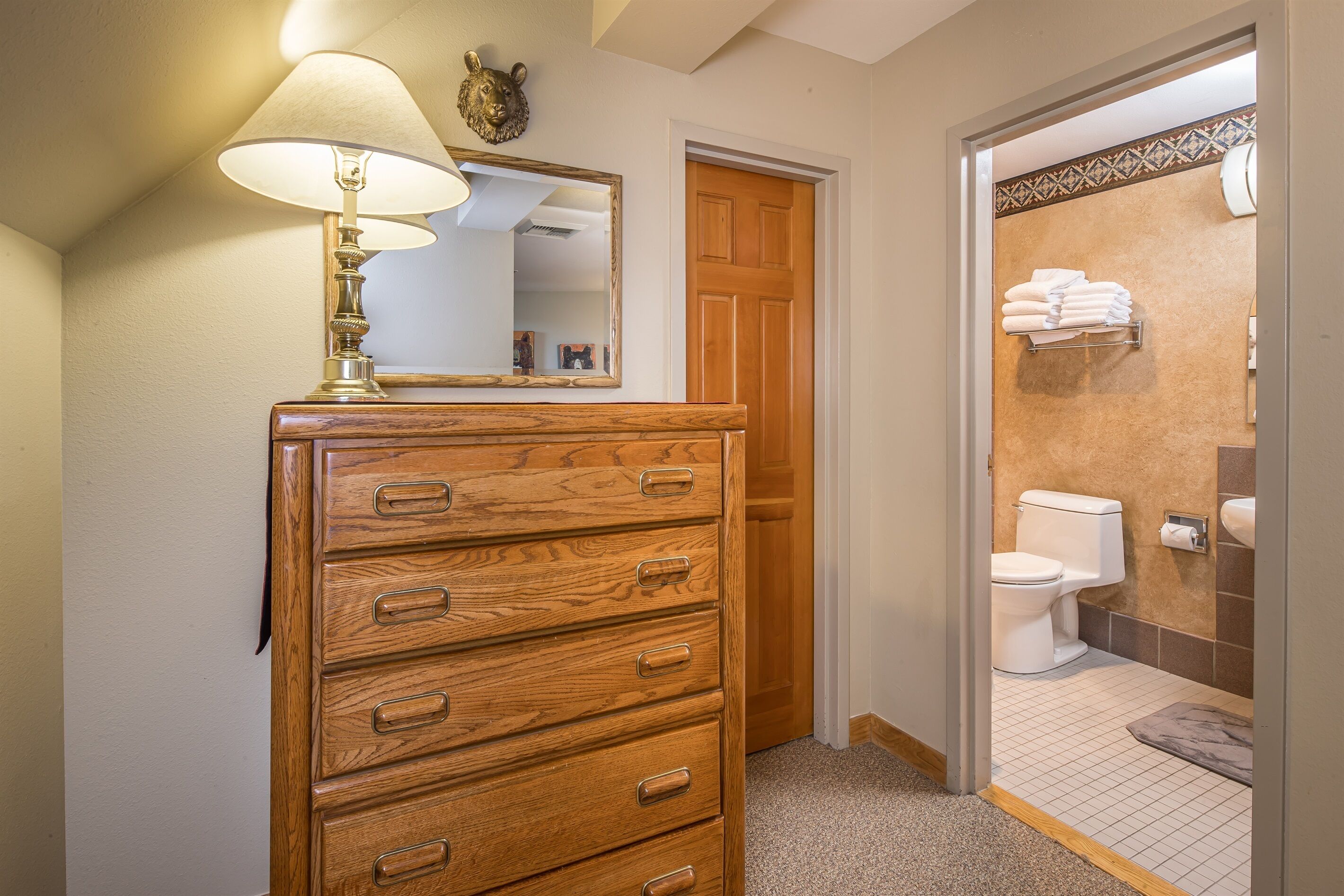 A wooden dresser with drawers, a mirror, and a lamp in a bathroom with a toilet and towel rack.