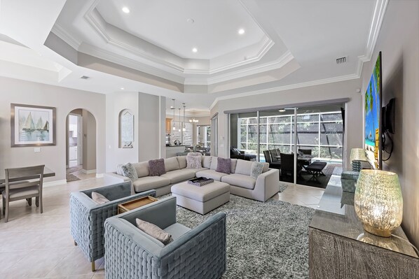 A spacious living room with a large sectional sofa, a dining area, and a view through a glass door to an outdoor pool area.