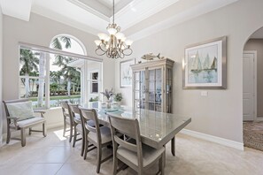 A dining area with a glass table, chairs, and a chandelier.