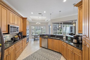 A modern kitchen with wooden cabinets, stainless steel appliances, and a large window providing a view of the outdoors.