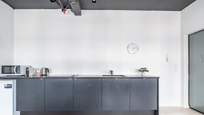 A modern kitchen with a dark countertop, a microwave, a coffee maker, and a clock on the wall.