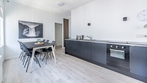 Une cuisine moderne avec un coin repas, comprenant un grand îlot central, des meubles de rangement aux couleurs sombres et une horloge murale.