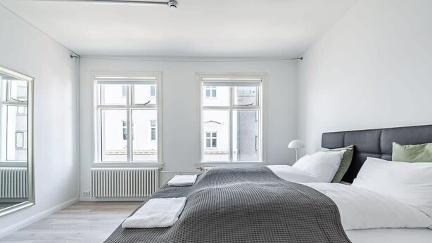 Une chambre moderne avec un grand lit, des murs blancs et deux fenêtres.