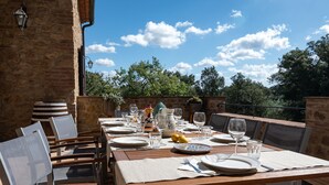 An outdoor dining area with a stone wall, wooden table, and chairs. - Romantic Villa with private pool - Il Pollaio (Volterra)