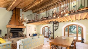 A spacious living area with a high ceiling, a fireplace, a sofa, a dining table, and a staircase leading to an upper level. - Romantic Villa with private pool - Il Pollaio (Volterra)
