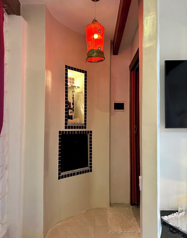 A hallway with a tiled floor, a red hanging light fixture, a mirror with a wine bottle, and a door with a red curtain.