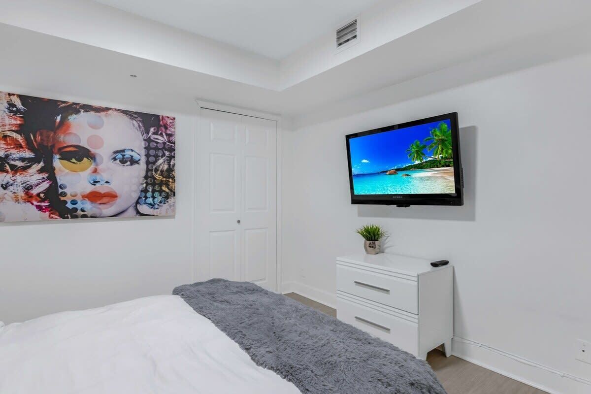 Une chambre à coucher avec un lit, un téléviseur fixé au mur, une commode et une porte.