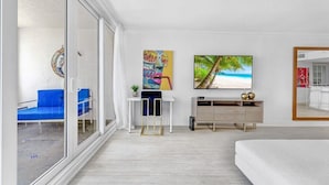 Une chambre d’hôtel moderne dotée d’une grande porte-fenêtre coulissante, d’un bureau blanc avec une chaise, d’un lit, d’une télévision et d’œuvres d’art accrochées au mur.