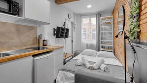 A compact hotel room with a kitchenette, a bed with towels, a TV, and a brick wall with greenery. - Getaway For 2, Beautiful Studio Near The Garonne (Toulouse)