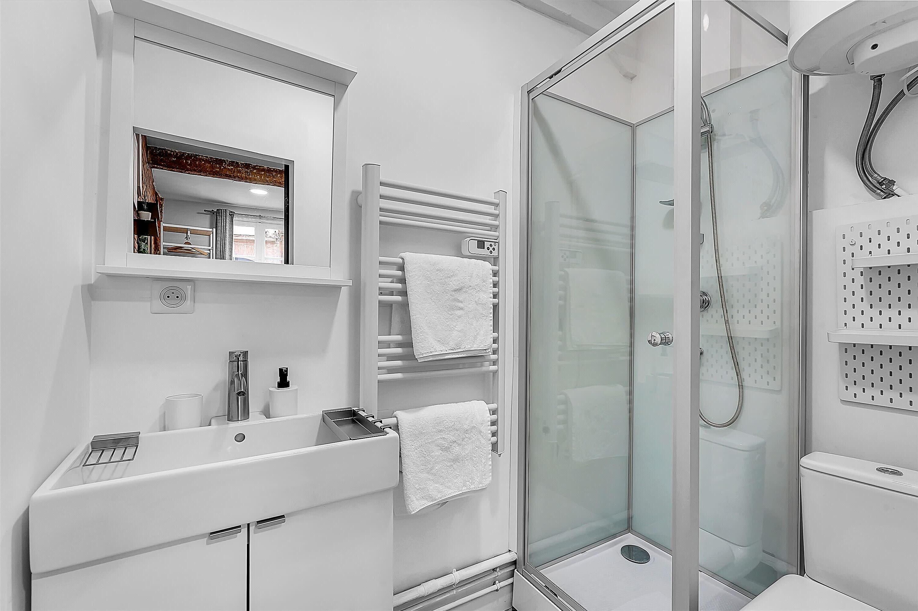 A modern bathroom with a glass-enclosed shower, a white sink with a mirror above it, and a towel rack with multiple towels.