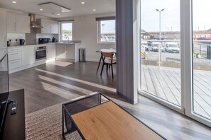 Una cocina moderna con armarios blancos, una zona de comedor con mesa y sillas, y ventanas amplias con vista a un estacionamiento.