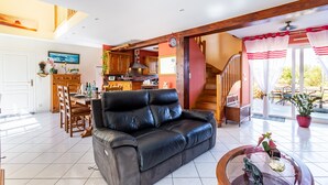 A spacious living room with a leather sofa, dining area, kitchen, and a staircase leading to an upper level.