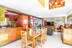 Una cocina amplia con armarios de madera, una mesa de comedor y sillas. Hay una pared de piedra y un televisor en la sala de estar.