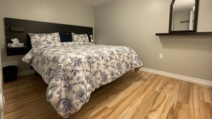 Una camera da letto con un letto, pavimento in legno, testiera, comodino e uno specchio a parete.