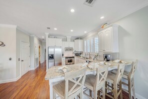 A modern kitchen with white cabinetry, a central island with bar stools, and a stainless steel refrigerator. - Large Laguna Beach Home Across from Beach w/Ground Floor Suite, FREE Perks! (Panama City Beach)