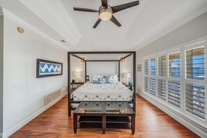 A four-poster bed with a canopy, bedside lamps, a framed picture on the wall, and a view through the window blinds. - Large Laguna Beach Home Across from Beach w/Ground Floor Suite, FREE Perks! (Panama City Beach)