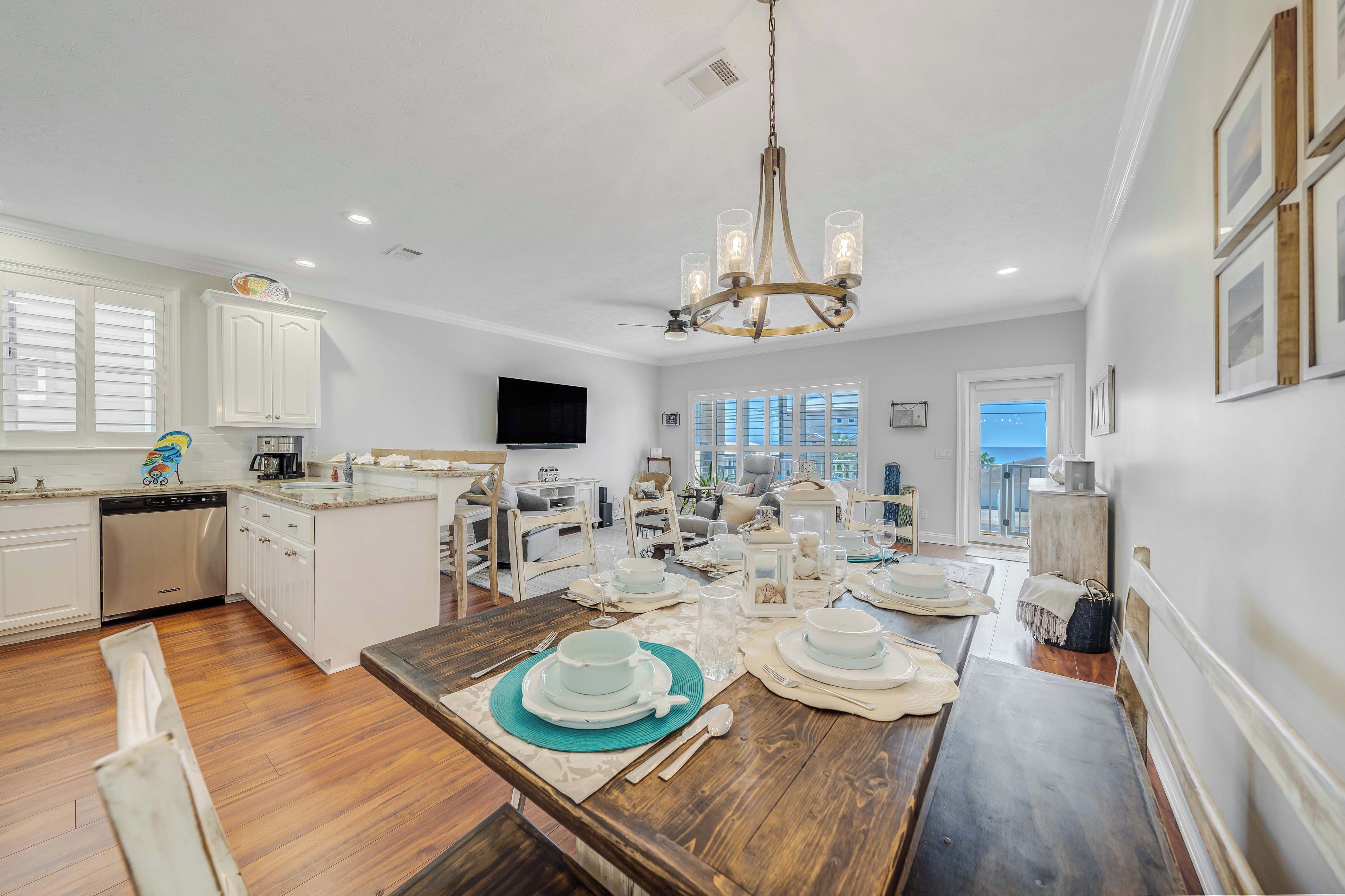 A spacious kitchen with wooden flooring, white cabinetry, and a central island. There is a dining area with a wooden table set for four, and a chandelier above.