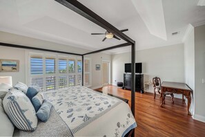 Ein Schlafzimmer mit einem großen Bett, einem Deckenventilator, einem Schreibtisch und Blick ins Freie.