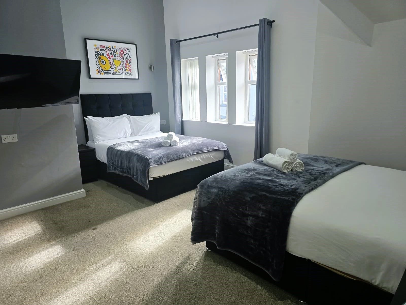A hotel room with two beds, a flat-screen TV, a window with curtains, and a wall-mounted artwork.