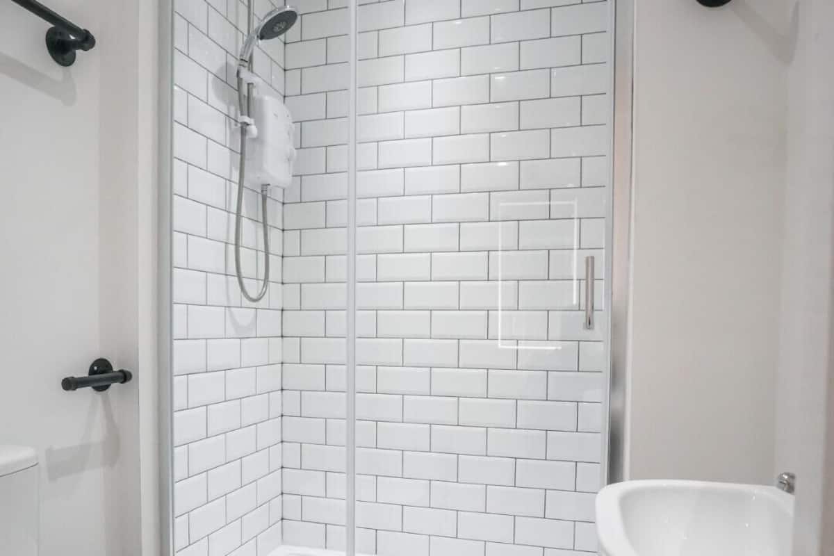 A bathroom with a glass-enclosed shower, white tiled walls, a white toilet, and a pedestal sink.