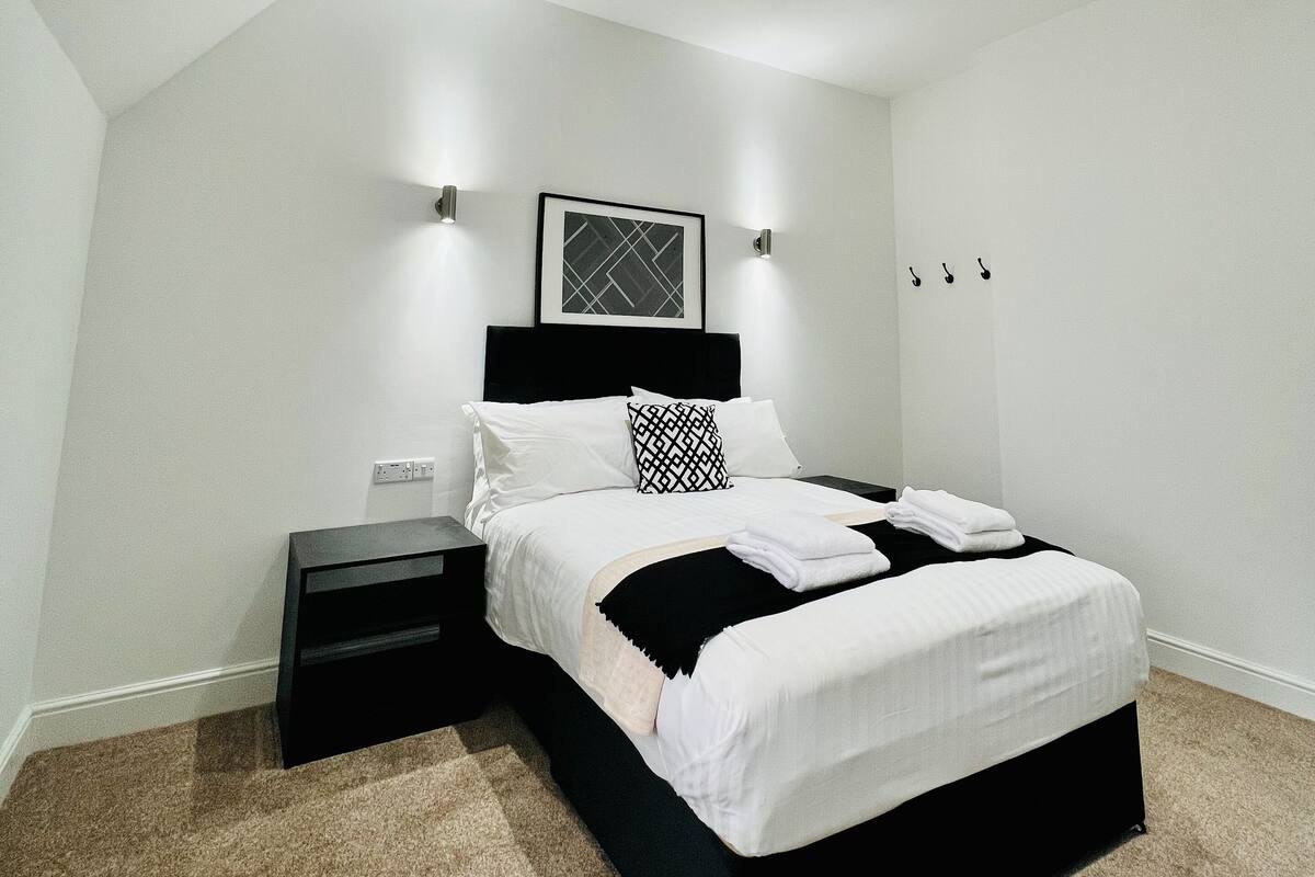 Un dormitorio moderno con cama bicolor, mesita de noche, cuadro en la pared y luces empotradas en el techo.