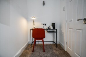 Ein kleiner, kompakter Raum mit einem roten Stuhl, einem Schreibtisch mit Lampe und einer Kaffeemaschine.